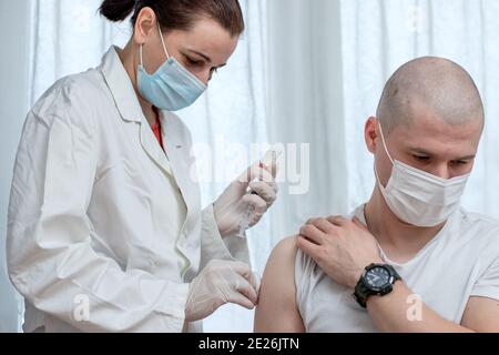 Ärztin injiziert männlichen Patienten mit Covid19 antiviralen Impfstoff. Massenimpfung und weltweite Impfkampagne. Nahaufnahme. Stockfoto