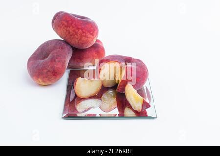 Nahaufnahme eines in Scheiben geschnittenen flachen Pfirsichs auf einer Glasoberfläche Isoliert auf weißem Hintergrund Stockfoto