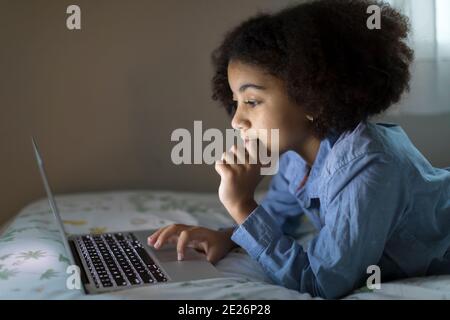 Seitenansicht eines zehn Jahre alten birassischen Mädchens, das an der Arbeit arbeitet Ihr Laptop Stockfoto