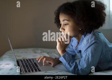 Seitenansicht eines zehn Jahre alten birassischen Mädchens, das an der Arbeit arbeitet Ihr Laptop Stockfoto