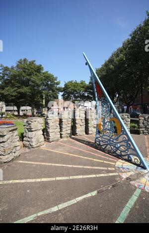 Prestwick Cross, Prestwick, Ayrshire, Schottland. VEREINIGTES KÖNIGREICH. Die ungewöhnliche Sonnenuhr zeigt von 4 bis 20 Uhr in Stunden. Stundenmarkierungen sind auf Steinsäulen mit Motiven, die lokale Interessen bezeichnen. Großer durchbohrter Gnomon mit aufwendigen Sonne, Mond, Sternen und Tierkreiszeichen. Die Platte ist von concre &tiles und bildet eine grobe Karte des Firth von Clyde, mit der Insel von Arran und einigen Straßen auf dem Festland. Die Sonnenuhr wurde von Kunststudenten des 6. Jahrgangs der Prestwick Academy mit Unterstützung von Mitgliedern der Kunstabteilung konzipiert und gestaltet, die in Zusammenarbeit mit der Künstlerin Elspeth Bennie aus Balfron arbeiteten. Stockfoto