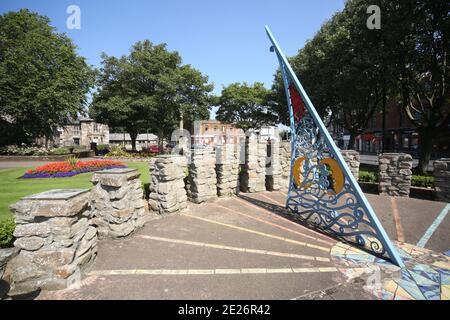 Prestwick Cross, Prestwick, Ayrshire, Schottland. VEREINIGTES KÖNIGREICH. Die ungewöhnliche Sonnenuhr zeigt von 4 bis 20 Uhr in Stunden. Stundenmarkierungen sind auf Steinsäulen mit Motiven, die lokale Interessen bezeichnen. Großer durchbohrter Gnomon mit aufwendigen Sonne, Mond, Sternen und Tierkreiszeichen. Die Platte ist von concre &tiles und bildet eine grobe Karte des Firth von Clyde, mit der Insel von Arran und einigen Straßen auf dem Festland. Die Sonnenuhr wurde von Kunststudenten des 6. Jahrgangs der Prestwick Academy mit Unterstützung von Mitgliedern der Kunstabteilung konzipiert und gestaltet, die in Zusammenarbeit mit der Künstlerin Elspeth Bennie aus Balfron arbeiteten. Stockfoto