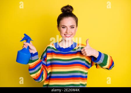 Foto von attraktiven Brünette bun junge Frau halten Pulverizer zeigen Daumen nach oben empfehlen Produkt isoliert auf gelbem Hintergrund Stockfoto