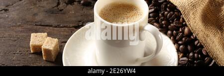 tasse Kaffee Espresso in weißem Porzellan Tasse mit gerösteten Kaffeebohnen auf altem Holzhintergrund mit Leinenbeutel Stockfoto