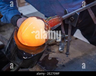 Glasbläser verwendet nasse Holzform für die Formung des roten geschmolzenen Glases am Ende des Glasblasrohres. Traditionelle tschechische Glaswerkstatt in Ku Stockfoto