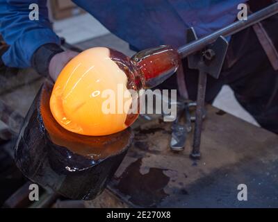 Handwerkliche Hände arbeiten mit heißem formbarem Glas auf Glasbläserpfeife. Traditionelle Glasformtechnik. Handgemachtes Glasstudio in Kunratice. Stockfoto