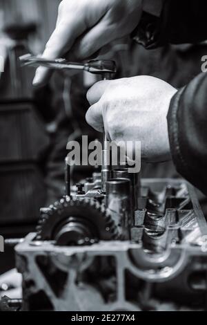 Hände eines Arbeiters, der einen Automotor in geringer Schärfentiefe repariert. Schwarzweiß-Fotografie Stockfoto