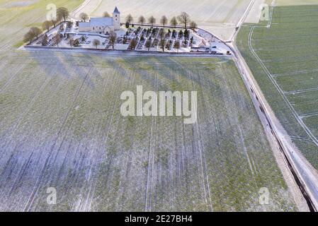 Eine typische altmodische Kirche, umgeben von Bauernhöfen und Winterbäumen. Stockfoto