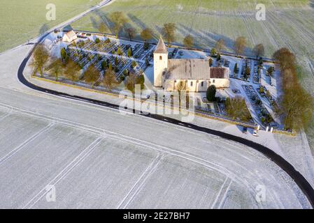 Eine typische altmodische Kirche, umgeben von Bauernhöfen und Winterbäumen. Stockfoto