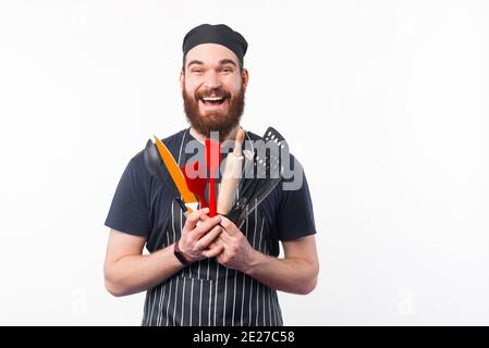 Foto von staunenden bärtigen Chef Mann hält Utensilien in der Hand. Stockfoto