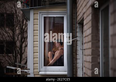 Ein liebevolles junges Paar umarmt sich im Fenster ihrer Balkonterrasse in der Wohnung. Der junge Mann lacht mit einer schönen Frau zu Hause. Liebhaber küssen, Pass Stockfoto