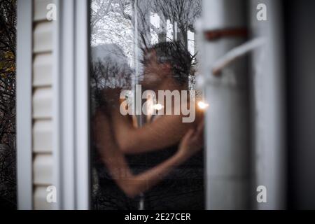 Ein liebevolles junges Paar umarmt sich im Fenster ihrer Balkonterrasse in der Wohnung. Der junge Mann lacht mit einer schönen Frau zu Hause. Liebhaber küssen, Pass Stockfoto