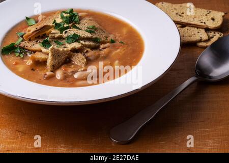 Schüssel mit Tomatenlinsensuppe mit Bohnen und dünnen knackigen Toasts auf Holzbrett Hintergrund. Vegane Mahlzeit, pflanzliche Nahrung Stockfoto