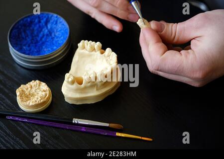 Der Zahntechniker beschäftigt sich mit der Modellierung von künstlichem Zahnersatz. Qualitätskontrolle des Zahnhalses. Stockfoto