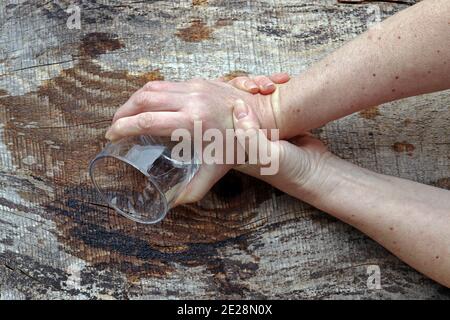 Eine Frau mit Parkinson schüttelt ihre Hände so stark, dass sie kein Glas mehr halten kann. Stark zitternde Hände einer älteren Frau Stockfoto