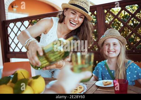 Glückliche junge Familie mit grünen Flasche Limonade und Teller von lokalen Bauernhof Zitronen beim Frühstück auf der Terrasse des Gästehaushotels. Stockfoto