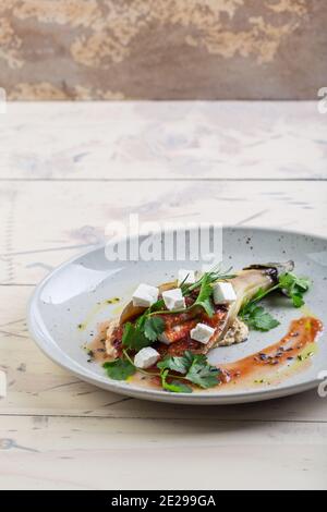 Saftige, appetitlich gebackene Aubergine mit Tomaten und Kräutern auf einem weißen Teller, serviert in einem Restaurant Stockfoto