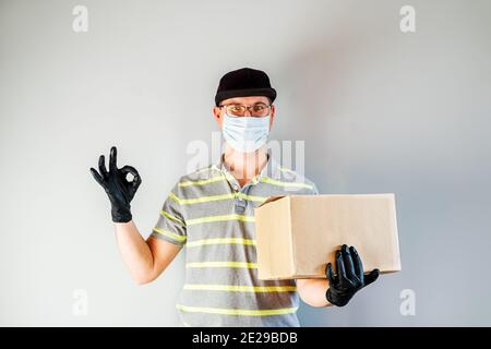 Delivery Service Mann in Schutzhandschuhe und Maske halten Karton-Box. Lieferservice, Online-Shopping und Logistikkonzept. Sichere Lieferung. Stockfoto