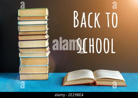 Zurück zur Schule Text auf schwarzer Tafel und offenes Buch, Stapel von Büchern auf blauem Tisch. Konzeptbildung. Vorderansicht. Stockfoto