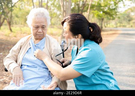 Arzt mit Stethoskop Überprüfung ältere oder ältere alte Dame Frau Patientin, während auf Rollstuhl im Park sitzen, gesund starke medizinische Konzept Stockfoto
