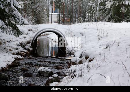 Ein Bach im Winter, der unter einer Straße fließt Stockfoto