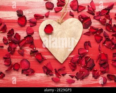 Rustikales Holzherz mit Rosenblättern auf roten Holzbohlen Stockfoto