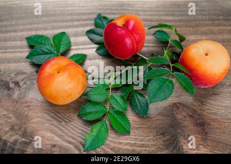Aprikosen mit frischen grünen Blättern auf einer Holzoberfläche Stockfoto