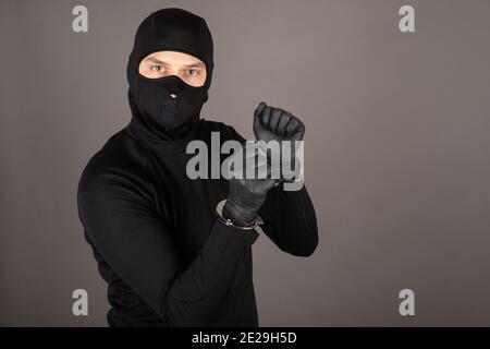 Dieb in schwarzem Anzug gekleidet und mit Maske auf seinem Gesicht posiert mit gefesselten Händen Stockfoto