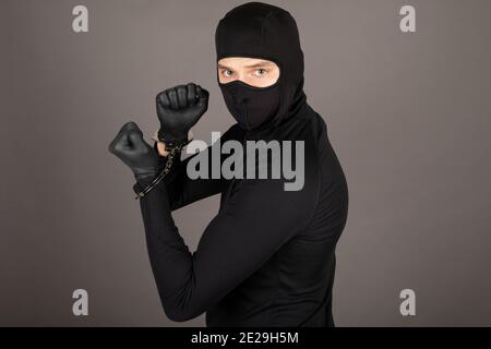 Dieb in schwarzem Anzug gekleidet und mit Maske auf seinem Gesicht posiert mit gefesselten Händen Stockfoto