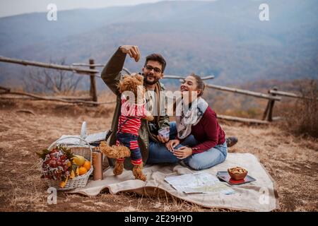 Pärchen beim Picknick auf der Decke sitzen und mit Hund spielen Neben ihnen Picknickkorb. Herbstzeit. Stockfoto