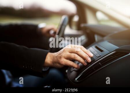 Geschäftsmann in Anzug ist die Anpassung einer Lautstärke auf seiner Stereoanlage während der Fahrt mit dem Auto. Stockfoto