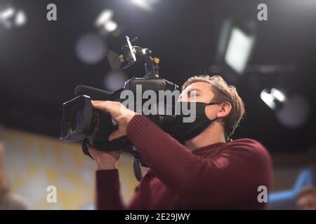 Maskierter Kameramann dreht eine Fernsehshow im Studio. TV Stockfoto