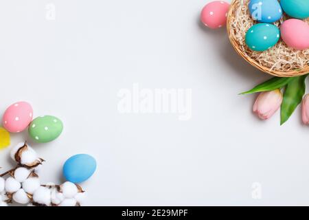 Frohe Ostern. Bunte Eier in einem Korb, Tulpen und ein Zweig aus Baumwolle auf einem grauen Hintergrund. Platz zum Kopieren von Grußkarten mit flachem Lay-Papier. Stockfoto