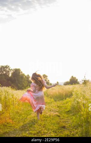 Mädchen läuft über das Feld in einem rosa Kleid Stockfoto