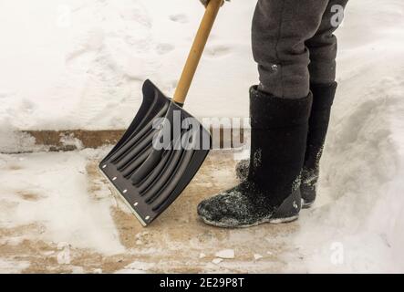 Ein Mann in Filzstiefeln, mit einer Schaufel in den Händen, entfernt nach einem Schneefall Schnee vom Bürgersteig. Stockfoto