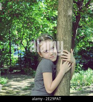 Konzept der jungen Mädchen umarmt einen Baum im Park, Vorderansicht Porträt Stockfoto