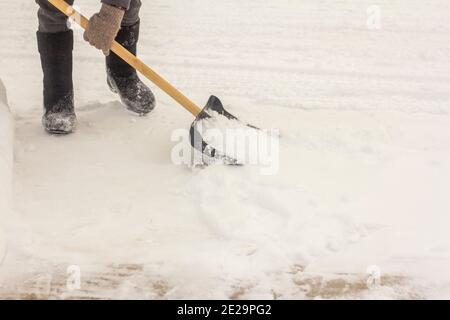 Ein Mann in Filzstiefeln, mit einer Schaufel in den Händen, entfernt nach einem Schneefall Schnee vom Bürgersteig. Stockfoto