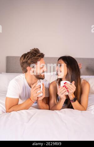 Vertikale Aufnahme des kaukasischen Paares mit Tasse Kaffee auf Ein Bett in einem Hotelzimmer Stockfoto