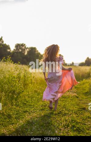 Mädchen läuft über das Feld in einem rosa Kleid Stockfoto