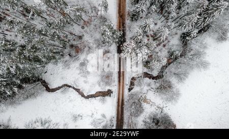 Ein schneebedeckter Winterwald, durch den ein kleiner Fluss fließt, ein Foto aus der Luft Stockfoto