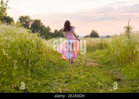 Mädchen läuft über das Feld in einem rosa Kleid Stockfoto