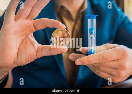 Geschäftsmänner Hände halten Gold Kryptowährung Bitcoin und Sanduhr. Kryptowährung und Bitcoin-Konzept. Stockfoto