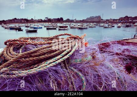 Normandie, Frankreich. Bunte Fischernetz trocknen auf Pier nach den Fischern wieder mit frischem Fang; Anlegeboote und Saint-Vaast-la-Hougue Häuser bei backgro Stockfoto