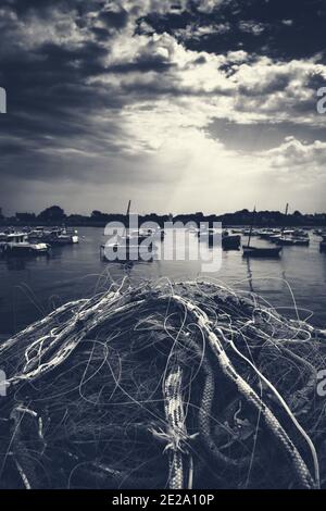 Normandie, Frankreich. Küstenlandschaft. Fischernetz trocknet auf Pier nach den Fischern zurück mit frischem Fang; Festmachen Boote in der Bucht vor einem Sturm. Dunkles Monoc Stockfoto