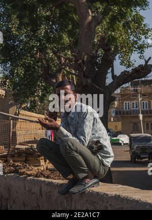 Jaisalmer, Rajasthan / Indien - 8. Januar 2020 : Mann sitzt an einer Wand tut Multitasking, im Gespräch mit Handy Rauchen Zigarette Blick auf die Photogr Stockfoto