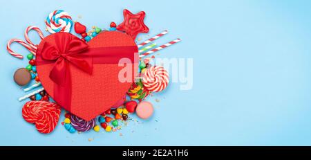 Verschiedene Süßigkeiten Sortiment und herzförmige Geschenkbox. Grußkarte zum Valentinstag. Süßigkeiten, Bonbon, Schokolade und Makronen auf blauem Hintergrund. Oben vi Stockfoto