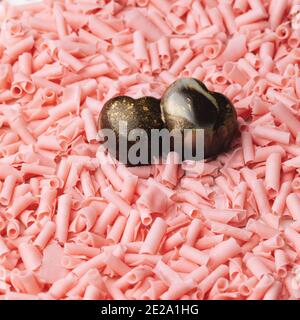 Fertigen Sie dunkle Schokolade Bonbons in einer doppelten Herzform auf Locken von rosa Schokolade. Süßes Geschenk für Valentinstag Stockfoto