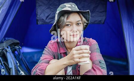 Junge asiatische Frau trinken Kaffee im Zelt Camping Stockfoto