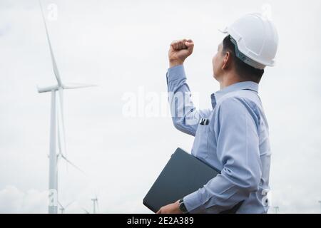 Ingenieure Windmühlen tragen Gesichtsmaske und arbeiten auf Laptop mit Die Windenergieanlage im Hintergrund Stockfoto