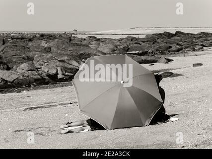 Normandie, Frankreich. Junges Paar, das sich am Strand unter einem Sonnenschirm entspannt. Sommer Urlaub am Strand Hintergrund. Nostalgie, glückliche Erinnerungen alte Zeiten Konzepte. S Stockfoto